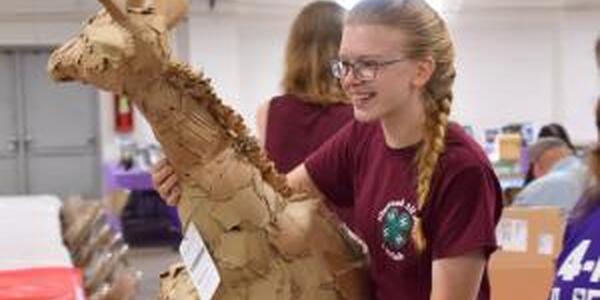 girl holding a 4-H visual arts project, paper machae giraffe